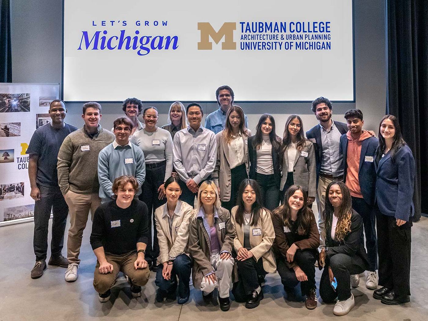 A student cohort beneath a Taubman College, University of Michigan banner